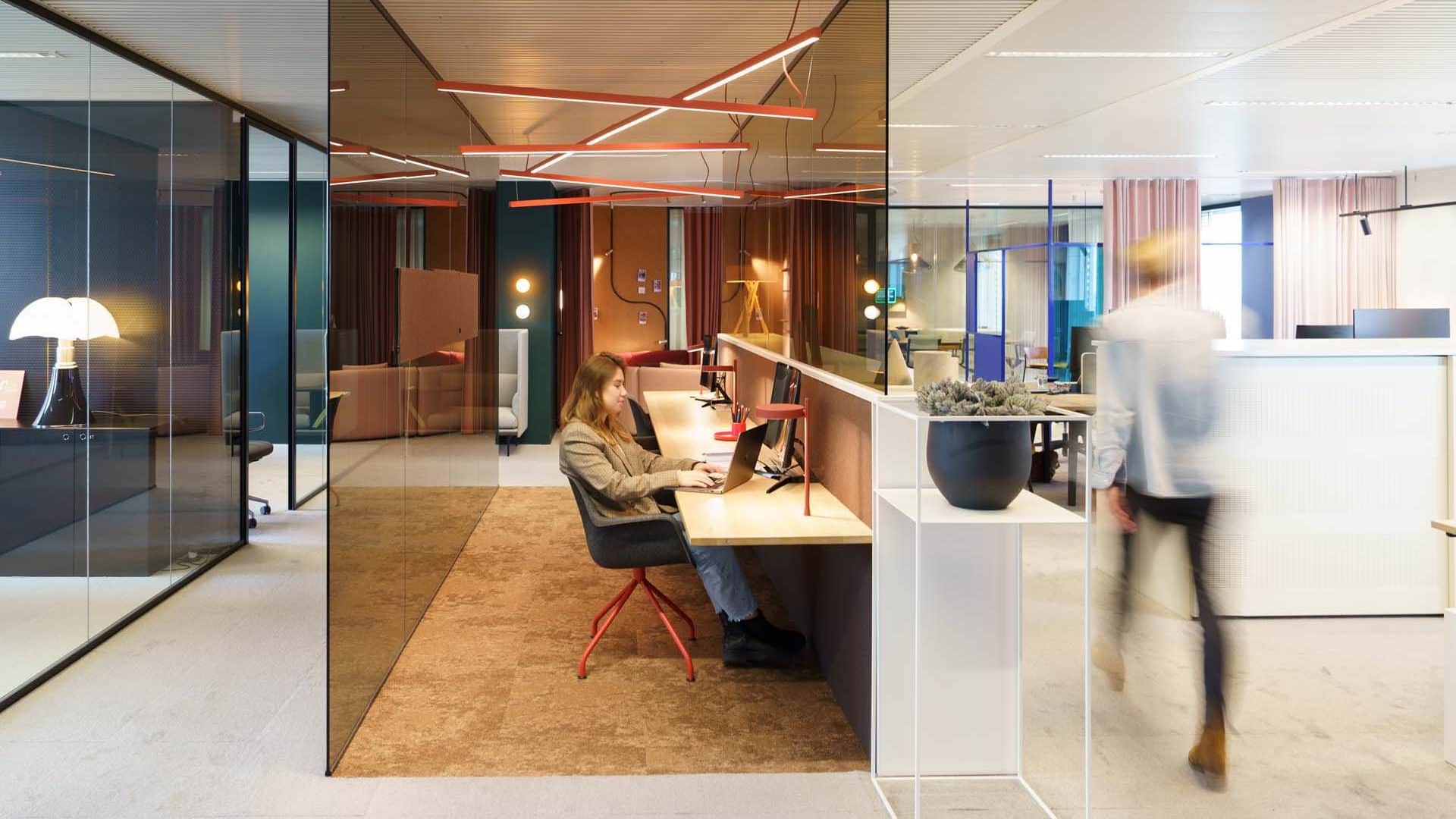 Medewerker werkt geconcentreerd aan flexwerkplek in open kantoorruimte met natuurlijke lichtinval