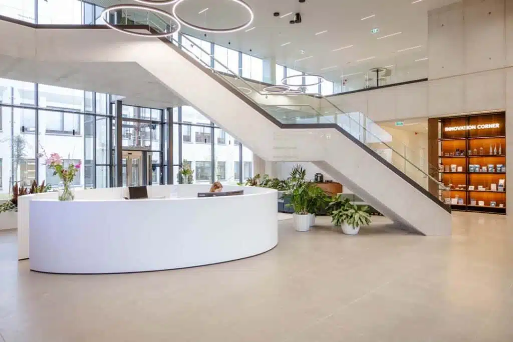Ruime inkomhal met ronde witte receptiebalie en moderne trapconstructie