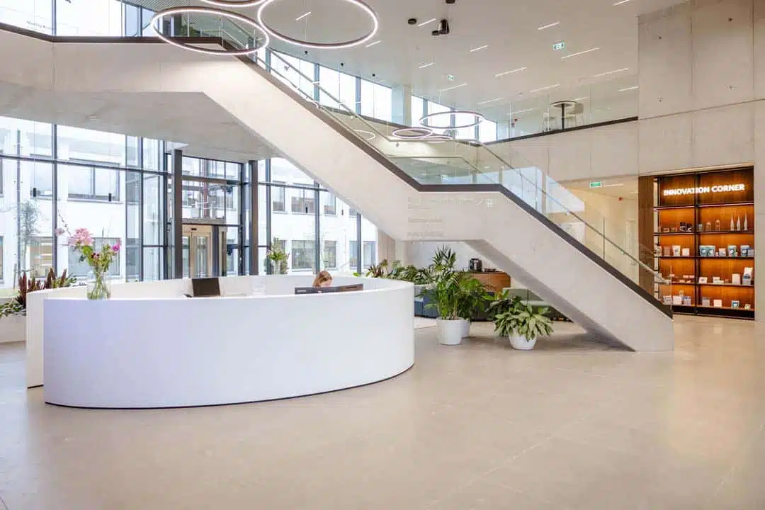 Ruime inkomhal met ronde witte receptiebalie en moderne trapconstructie