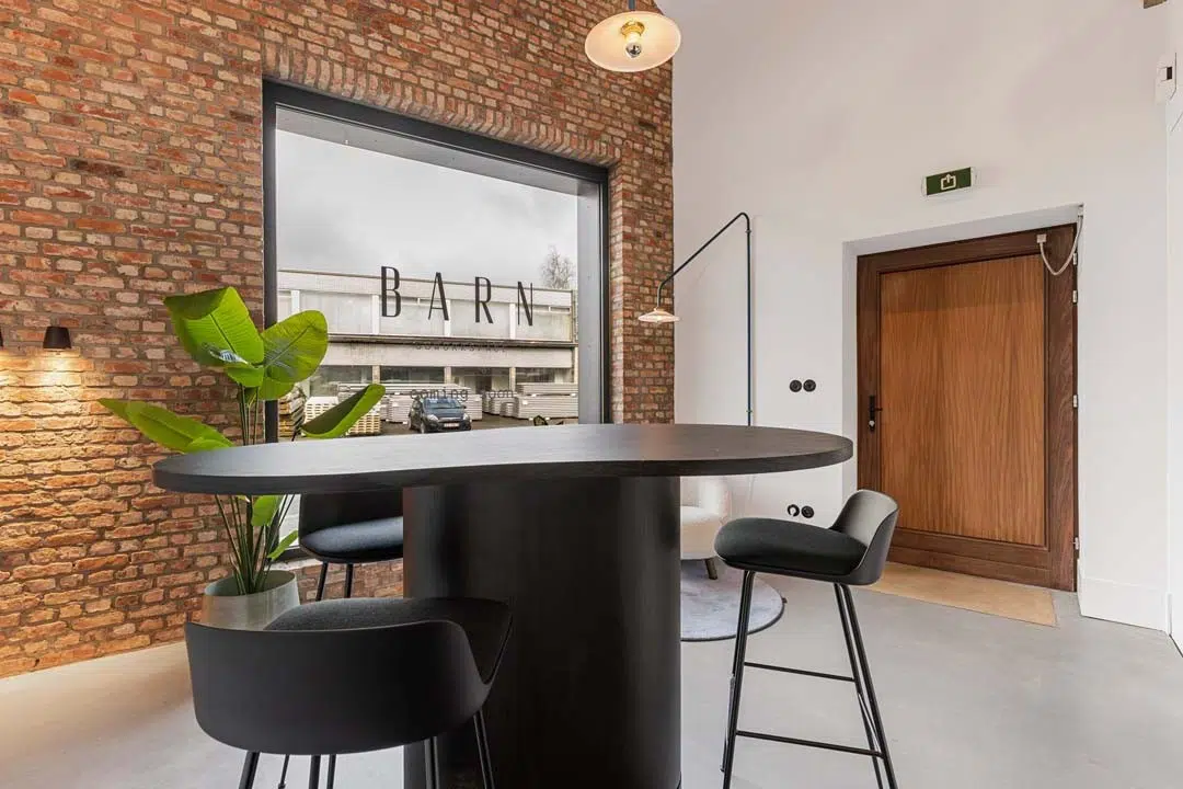 Onthaalzone met hoge tafel en bakstenen muur in Barn Coworking, ingericht door Buro Project