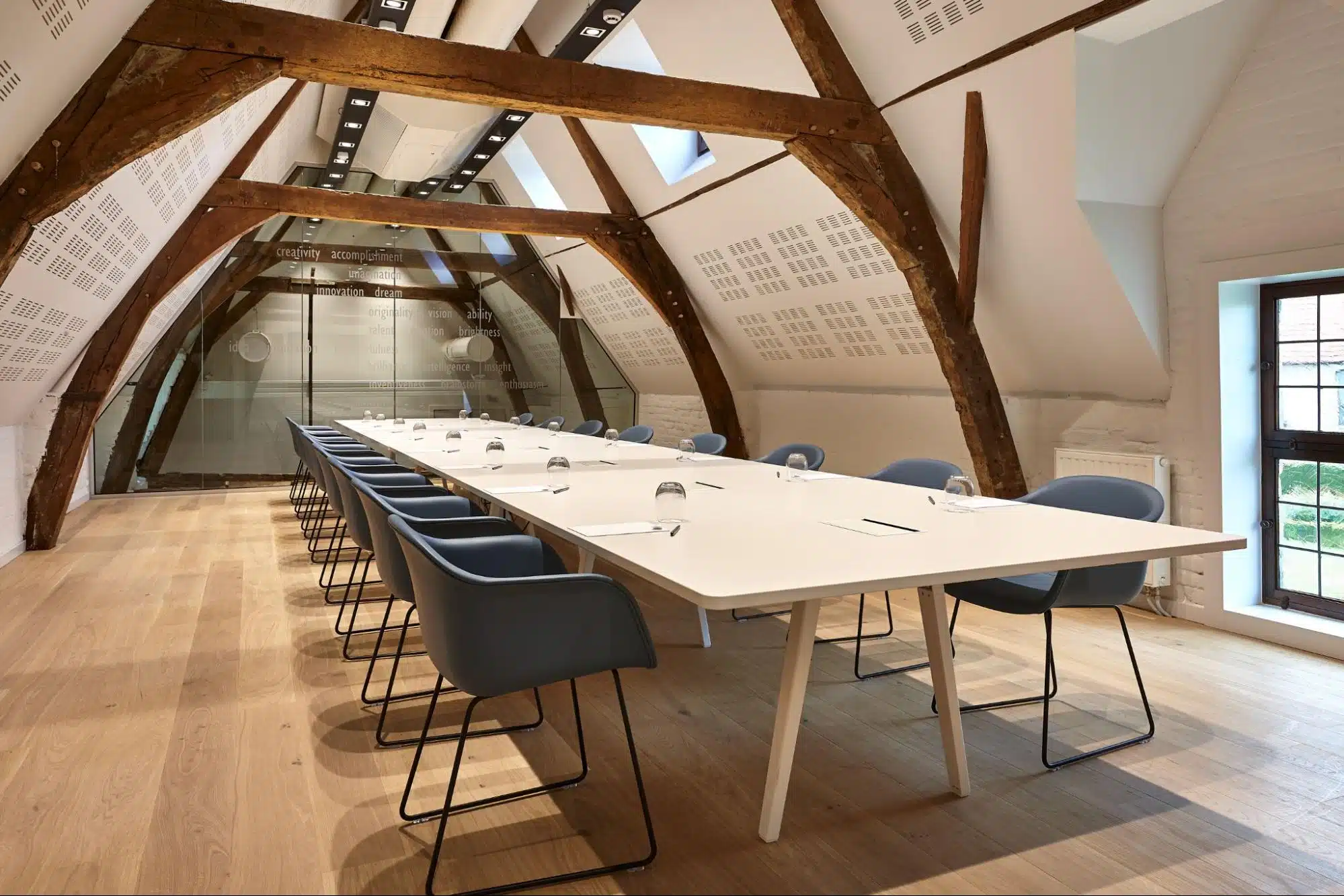 Vergaderzaal met lange tafel en moderne stoelen onder authentieke houten balken in een universiteit