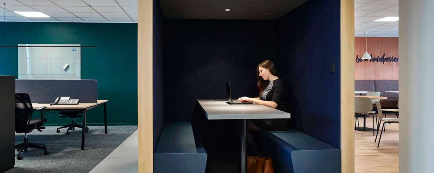 Vrouw werkt geconcentreerd in een akoestische werkpod in een open kantoorruimte voor meer rust en focus