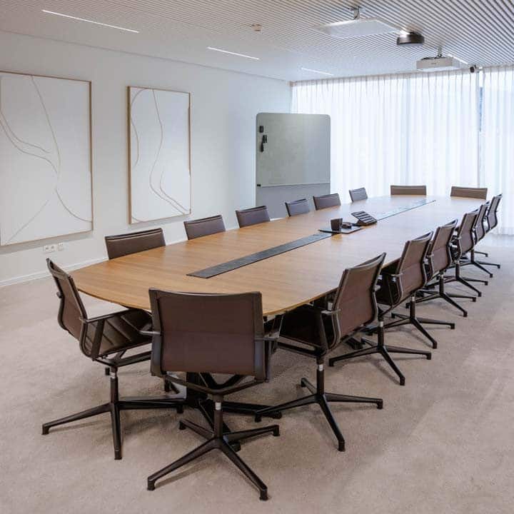 Moderne kantoorinrichting met grote vergadertafel en ergonomische bureaustoelen in een minimalistische vergaderruimte.
