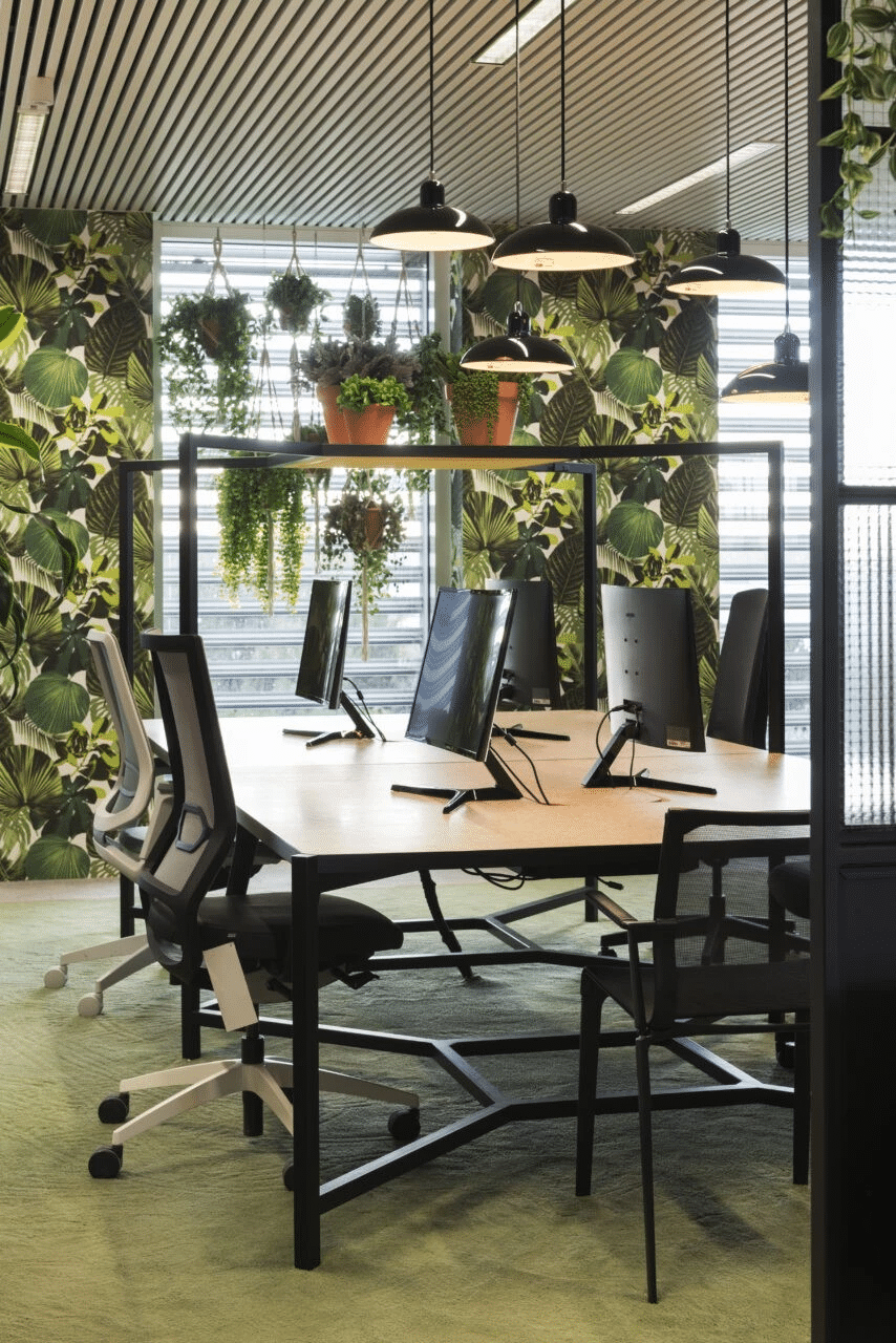 Moderne kantoorinrichting met werkplekken, hanglampen en groene planten die zorgen voor een inspirerende en natuurlijke werkomgeving.