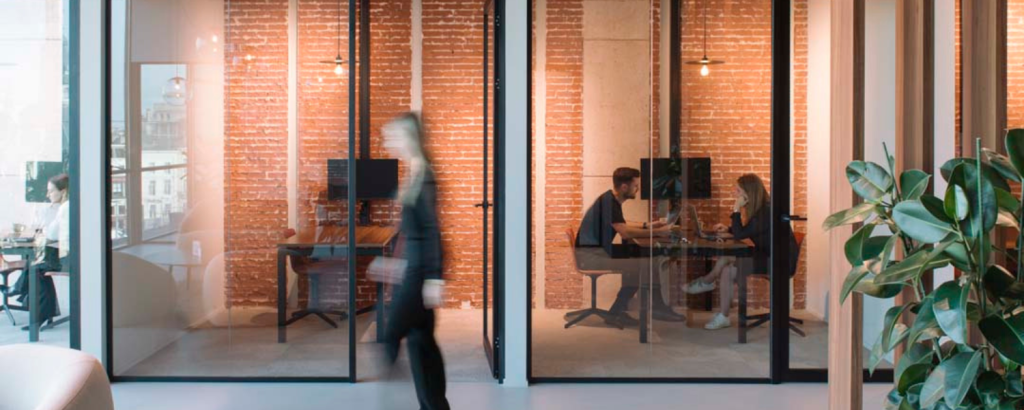 Espace de bureau moderne avec salles de réunion vitrées, postes de travail flexibles et collaborateurs travaillant ensemble dans un environnement de travail intelligent.