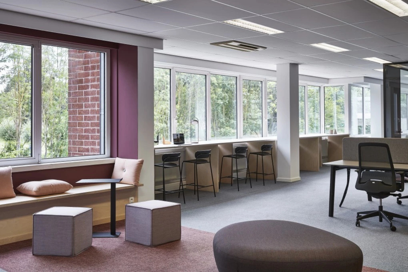 Lichte kantoorruimte met compacte barstoelen langs het raam en modulaire zitelementen die de ruimte functioneel houden zonder ze te overladen.