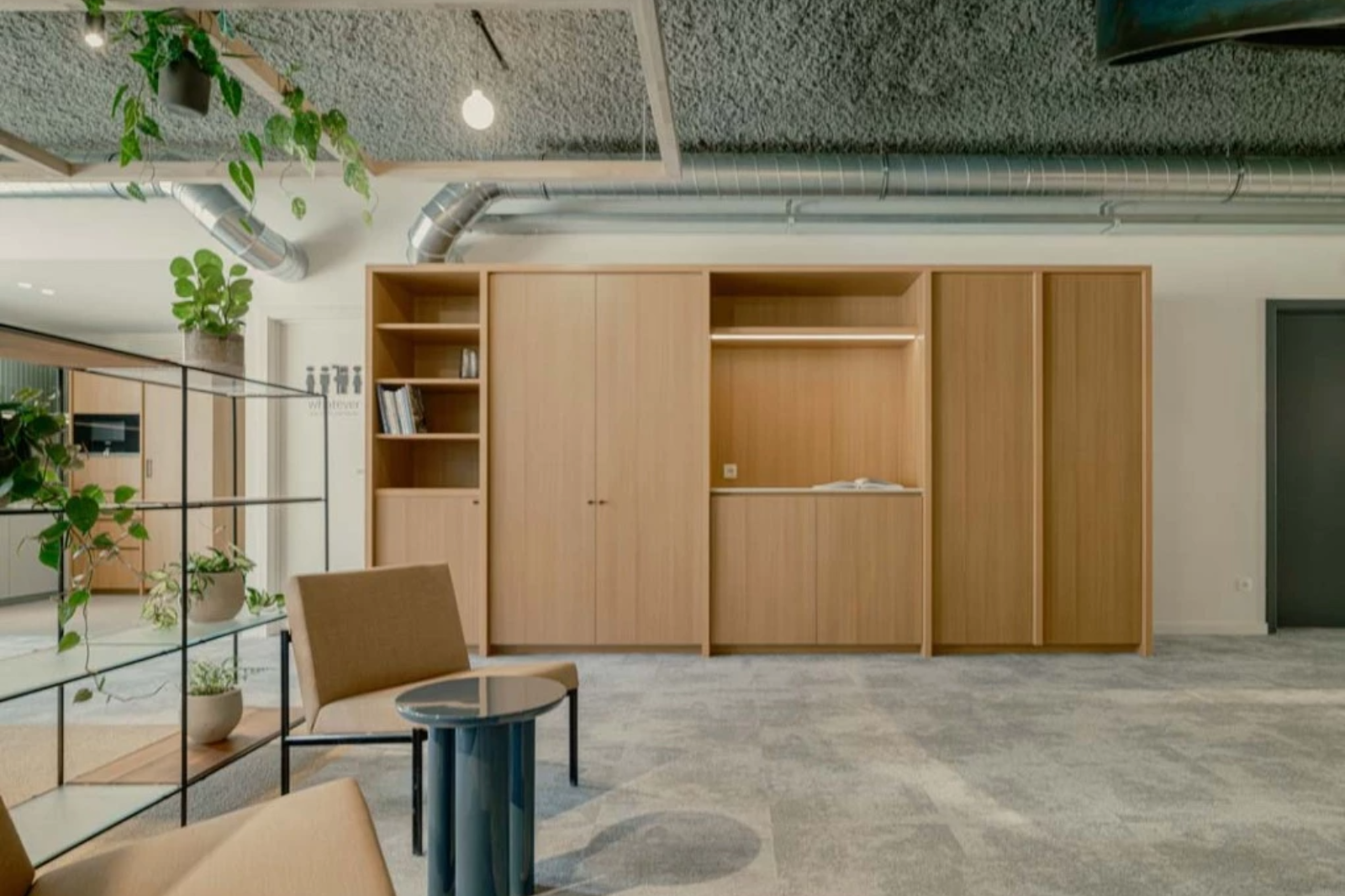 Strakke wand met gesloten houten kasten en open vakken die rust en orde creëren in een kleine kantoorruimte.