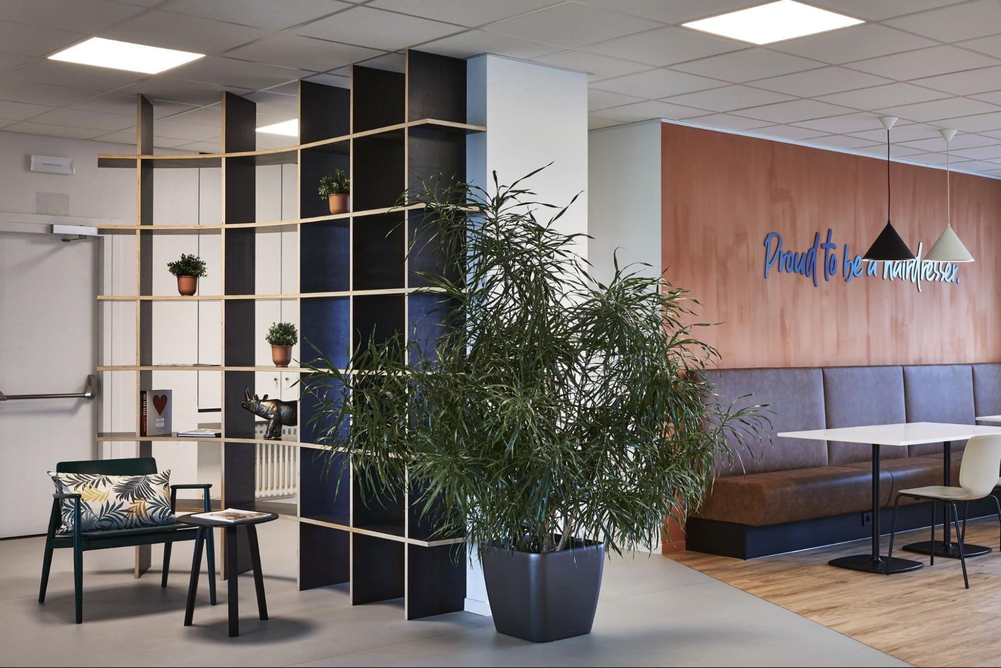 Hoog open rekensysteem als ruimteverdeler combineert verticale opbergruimte met planten voor een functionele en sfeervolle kantoorinrichting.