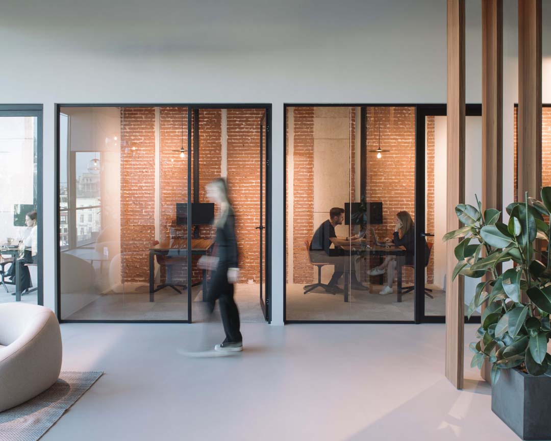 Open werkplekken met akoestische bureauschermen en glazen wanden die focus en geluidscomfort combineren.
