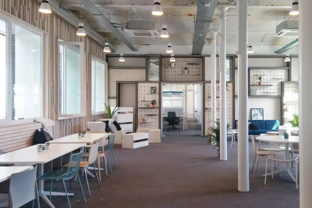 Open coworking space met lange tafels, lichte zones en flexibele werkplekken.
