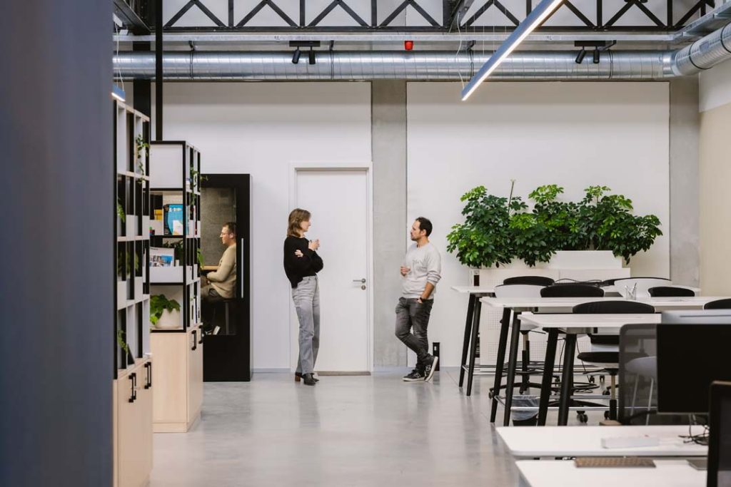 Collega's in gesprek naast een belcel in een open coworking space met veel groen.

