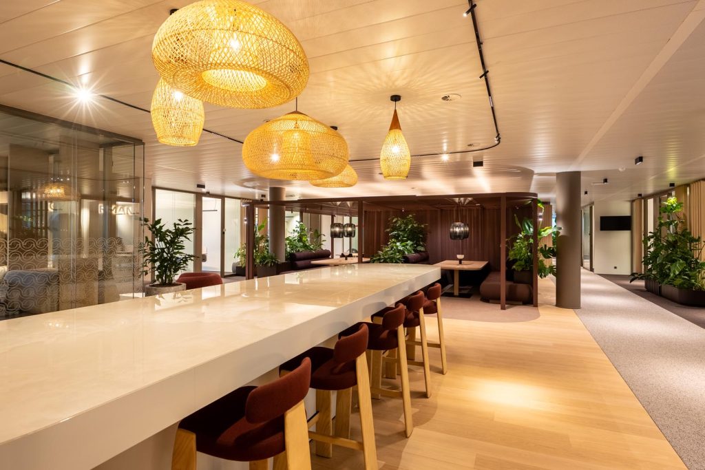 Lange bar met barkrukken en groen als sociale ontmoetingszone in een coworking space.