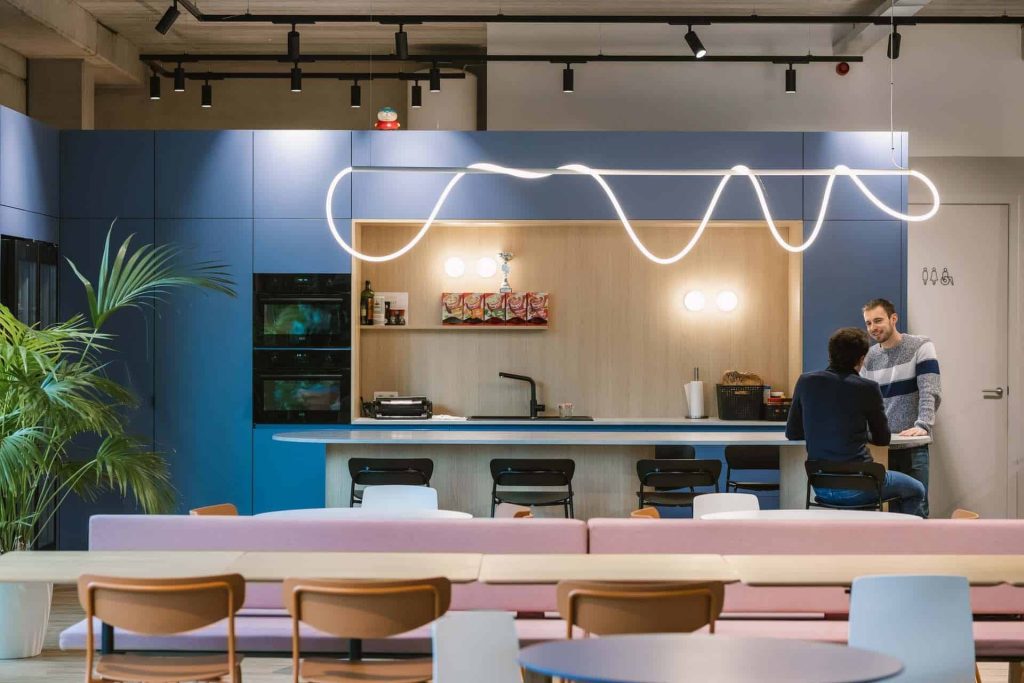 Collega's in gesprek aan de bar van een uitnodigende kantoorkeuken met zithoek, een informele ontmoetingsplek voor hybride teams.