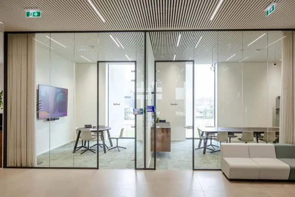 Glazen vergaderruimtes met een groot scherm, videobar en reservatieschermen aan de deur, voorbeeld van een kantoor waar technologie naadloos werkt.