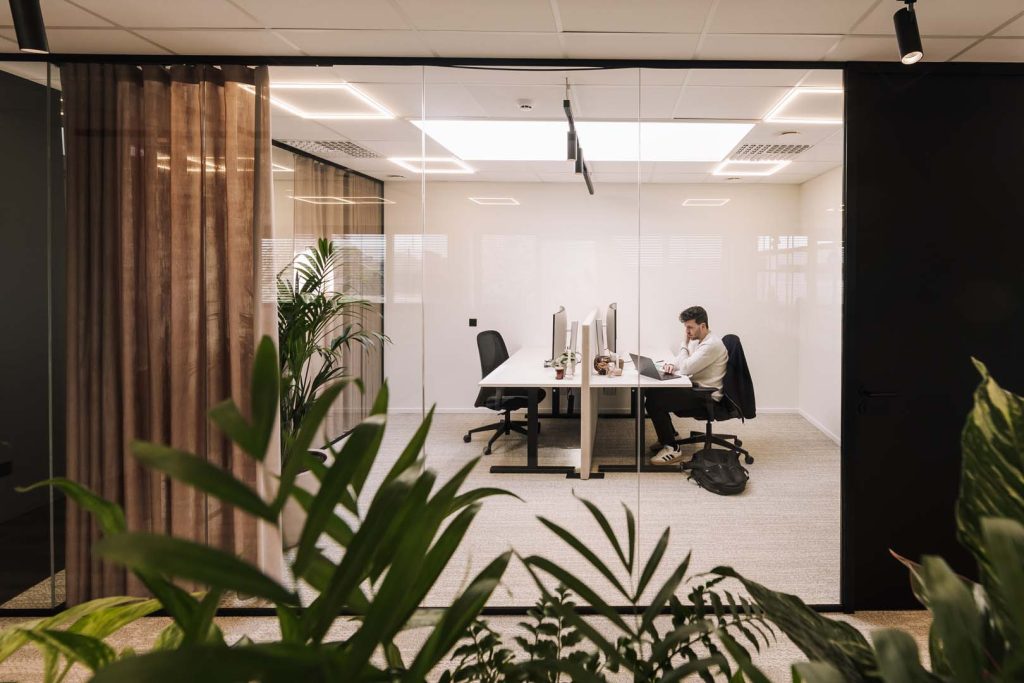 "Glazen kantoorruimte met flexwerkplekken waar een medewerker geconcentreerd werkt