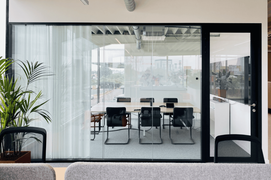 Glazen vergaderruimte met tafel, stoelen en videowall voor hybride overleg