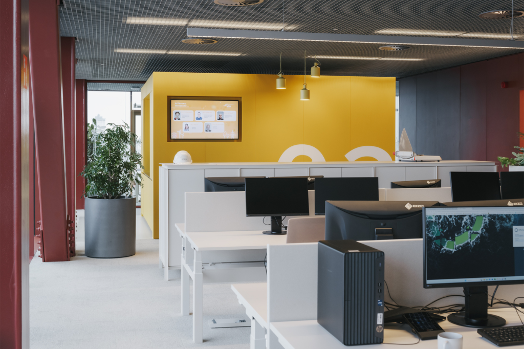 Kantoorzone met digitaal welkomstscherm en flexwerkplekken met dubbele monitoren