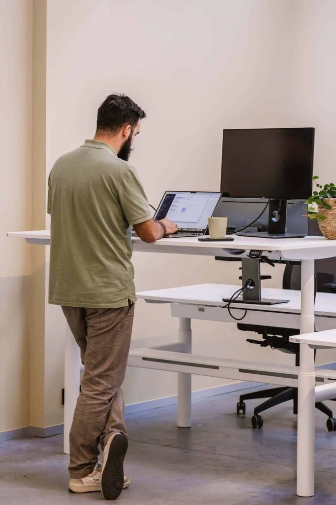 Man werkt staand aan een zit-sta bureau met laptop, extra scherm en opgeruimde werkplek